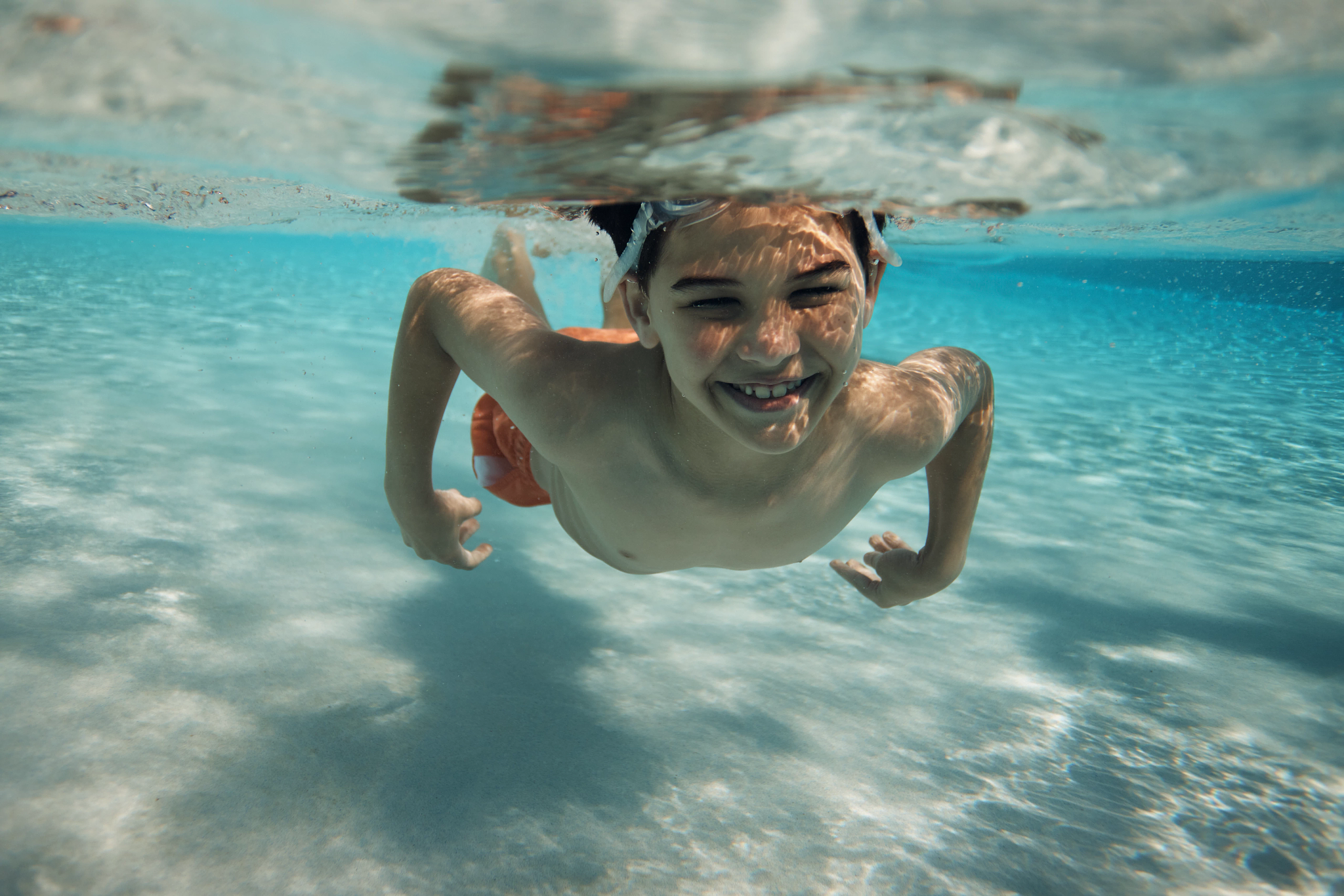 A young boy smiling underwater swimming towards the camera
