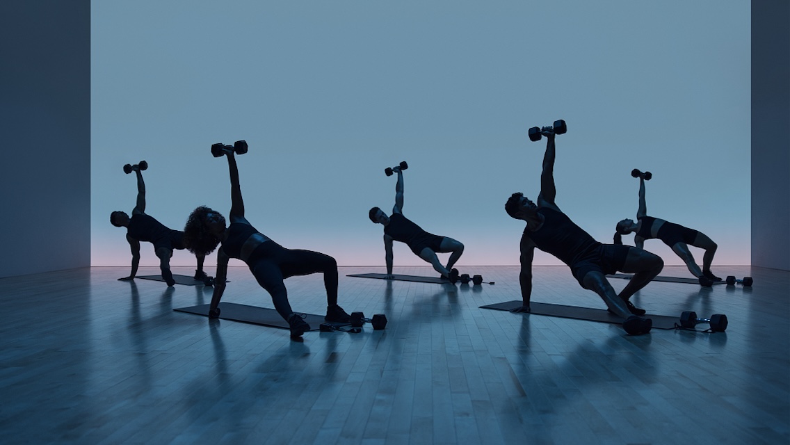 a group fitness class does a strength move holding a dumbbell overhead
